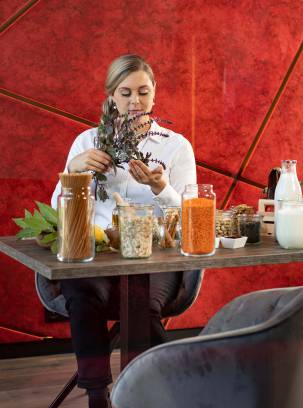 Eine Frau mit diversen natürlichen Lebensmitten sitzt an einem Tisch.