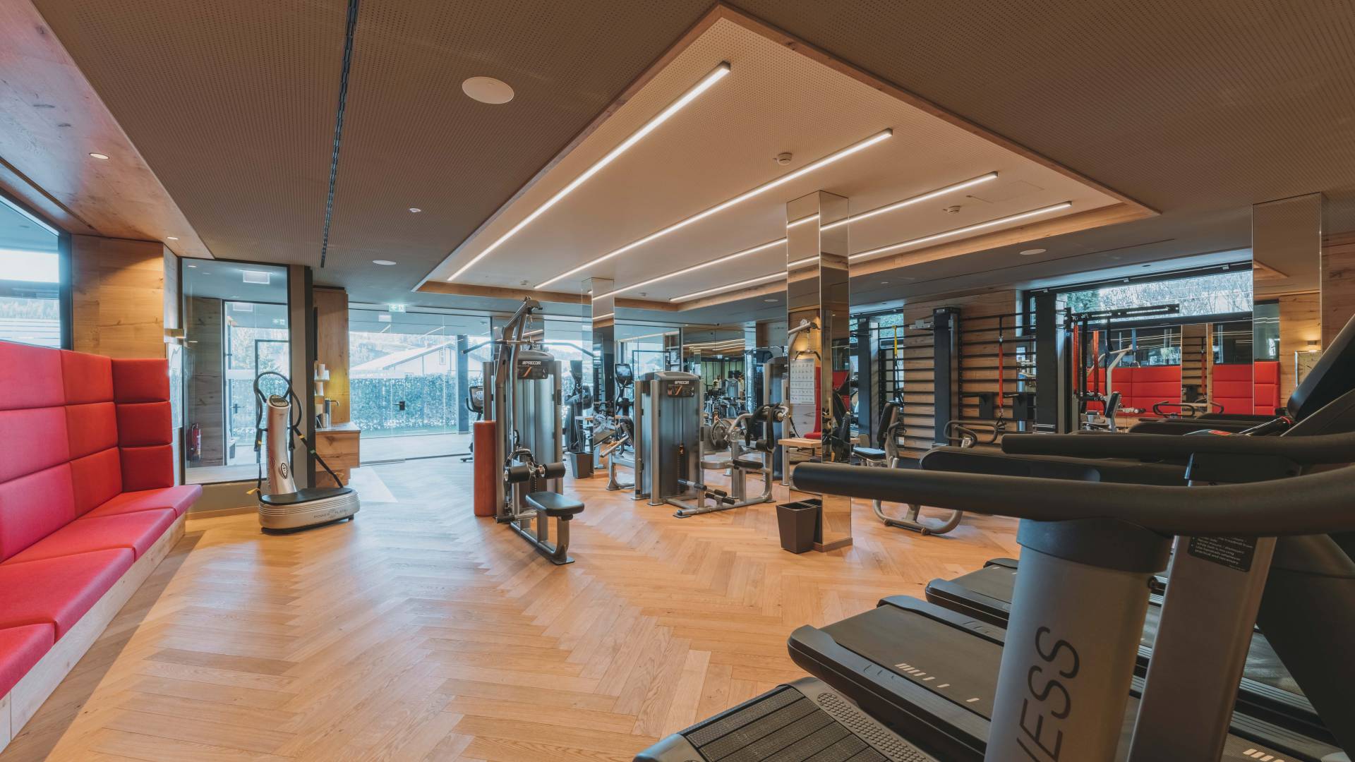 Modernes Fitnessstudio mit Holzboden und diversen Fitnessgeräten.