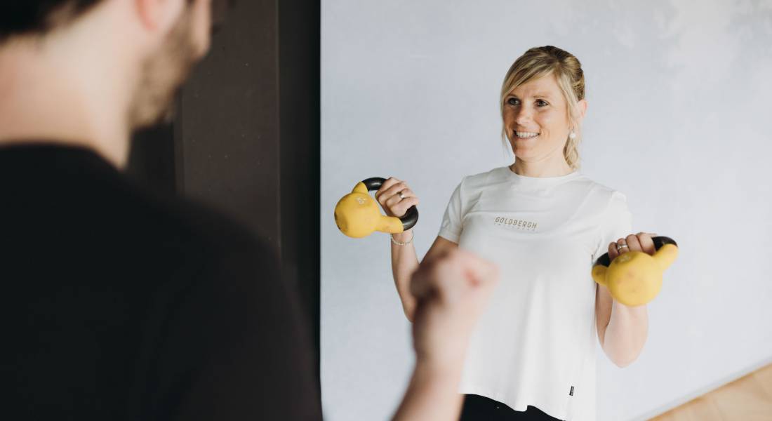 Eine junge Frau trainiert ihre Arme mit zwei Kettlebells.