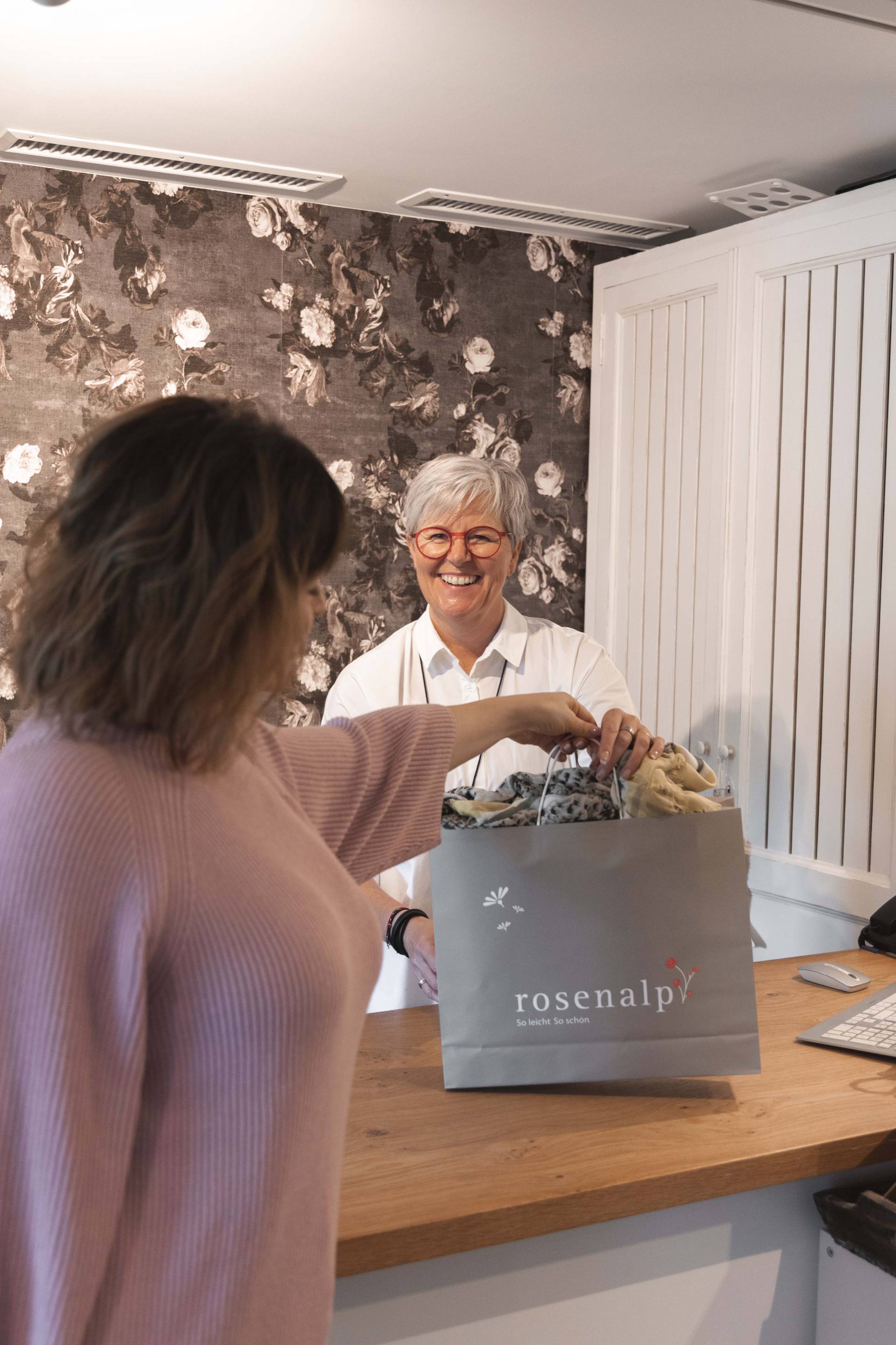 Eine Frau nimmt ihre Einkäufe in einer Tüte mit der Aufschrift "rosenalp" von der Verkäuferin entgegen.