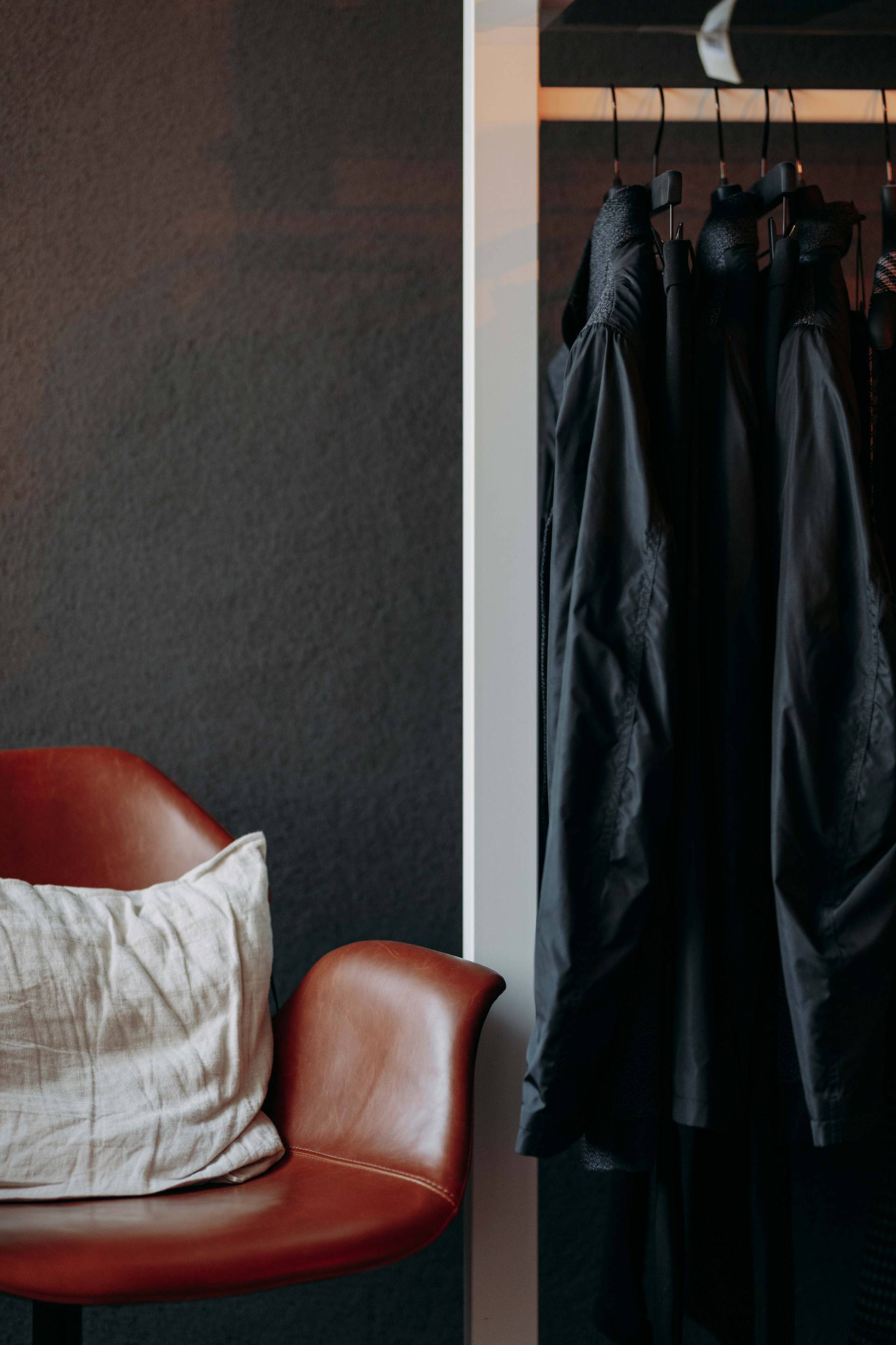 Einer Kleiderstange mit dunkler Mode neben einem Ledersessel.