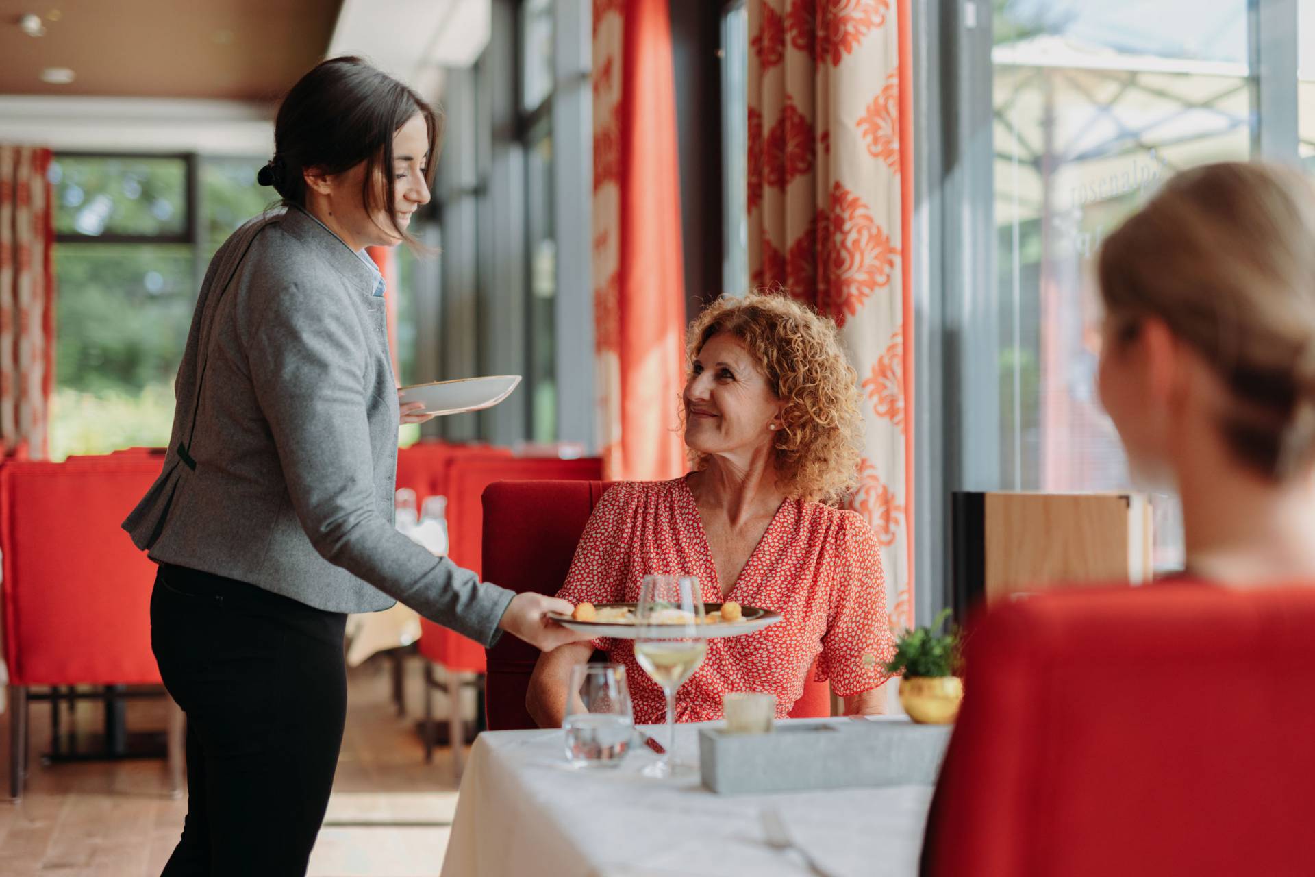 Zwei Frauen erhalten in einem Restaurant von der Kellnerin ihre Mahlzeiten.