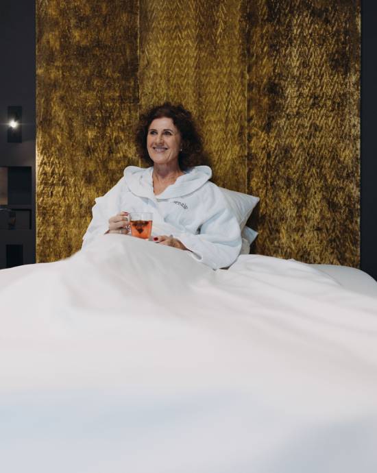 Eine Frau im Bademantel, die entspannt im Bett sitzt mit einer Tasse Tee in der Hand