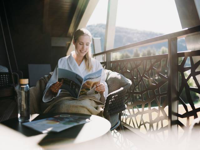 Eine Frau liest ein Magazin auf einem Sessel auf einem Balkon.