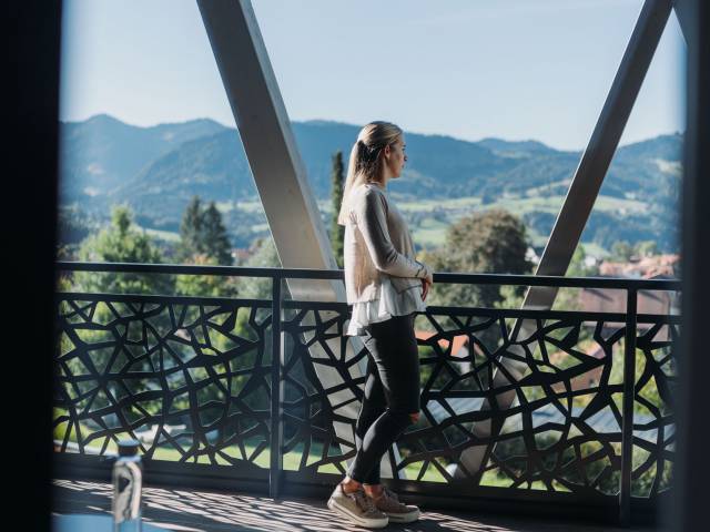 Eine Frau steht vor einem Bergpanorama auf einem Balkon als Teil einer Schrothkur in Oberstaufen.
