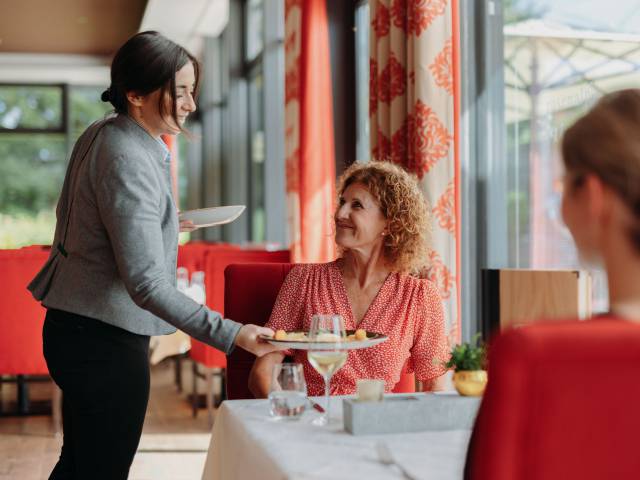 Zwei Frauen erhalten in einem Restaurant von der Kellnerin ihre Mahlzeiten.