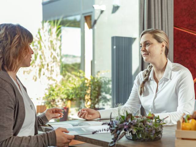 Zwei junge Frauen haben an einem Tisch ein beratendes Gespräch.