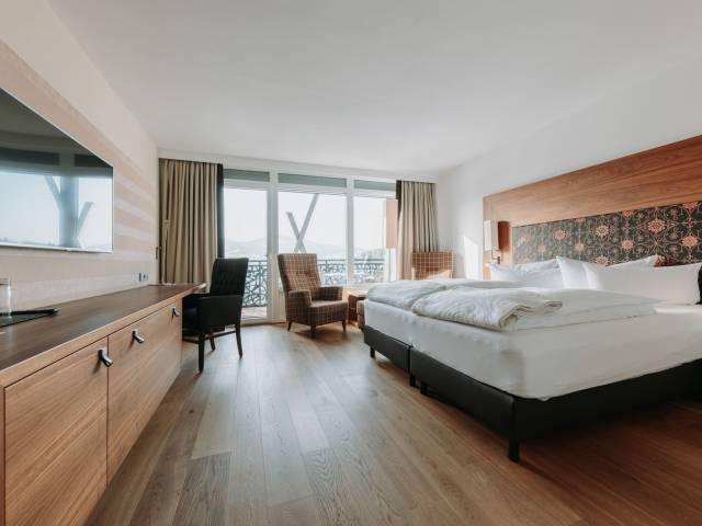 Sicht in ein modernes Hotelzimmer mit Doppelbett, Sesseln und großer Fensterfront.