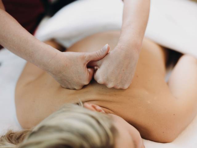 Eine Frau liegt auf dem Bauch auf einer Liege und bekommt eine Rückenmassage mit den Handknöcheln.