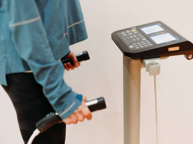 Frau mit 2 Griffen in der Hand, die an ein Messgerät angeschlossen sind