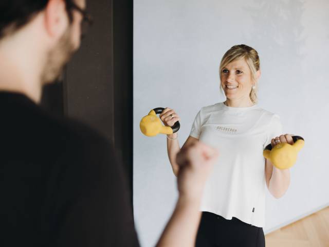 Eine Dame bei Training mit Kettlebells unter Beobachtung eines Trainiers