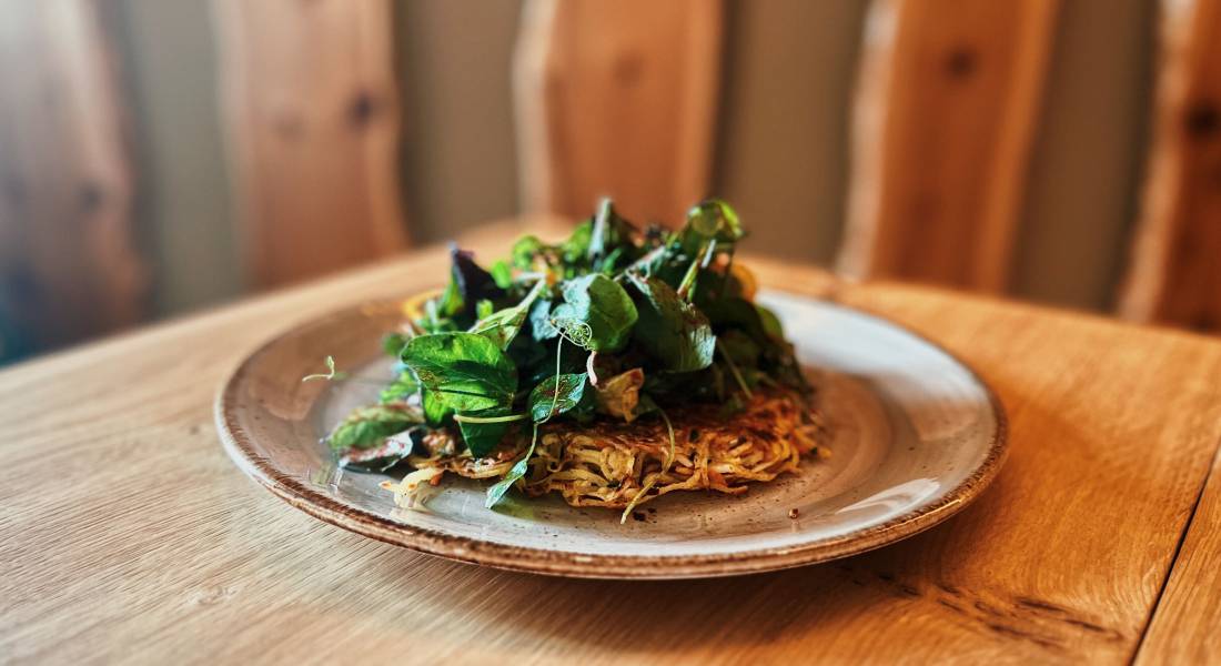 Gemüse-Kartoffelrösti auf einem naturfarbenen Teller steht auf einem Holztisch beim Ernährungsurlaub des Rosenalp Gesundheitsresort & Spa.
