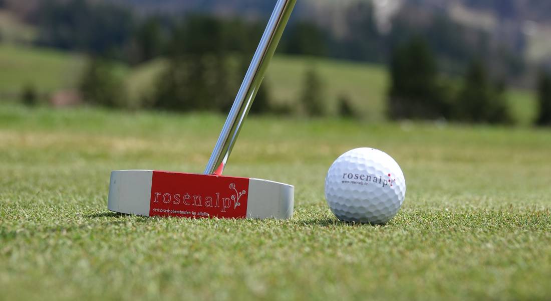 Nahaufnahme eines Putters und Golfballs mit der Aufschrift "rosenalp" auf Rasen als Teil eines Sommerurlaub in Bayern.