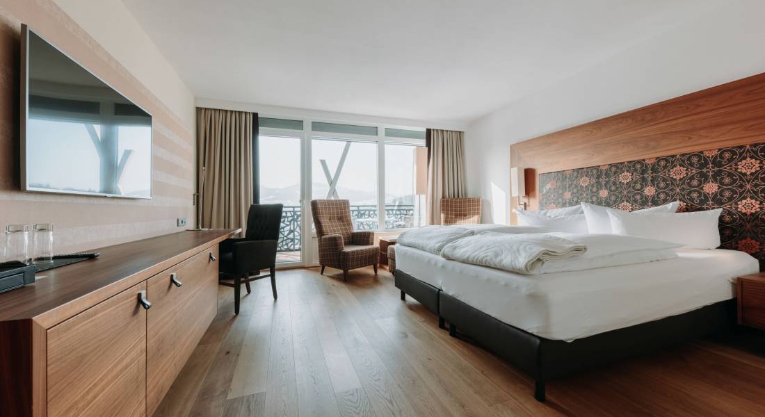 Sicht in ein modernes Hotelzimmer mit Doppelbett, Sesseln und großer Fensterfront.