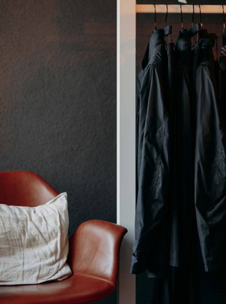 Einer Kleiderstange mit dunkler Mode neben einem Ledersessel.