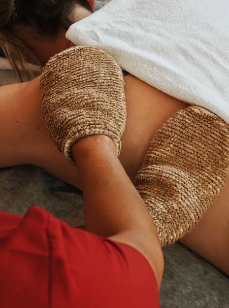 Eine auf dem Bauch liegende Frau erhält eine Behandlung mit Massagehandschuhen.