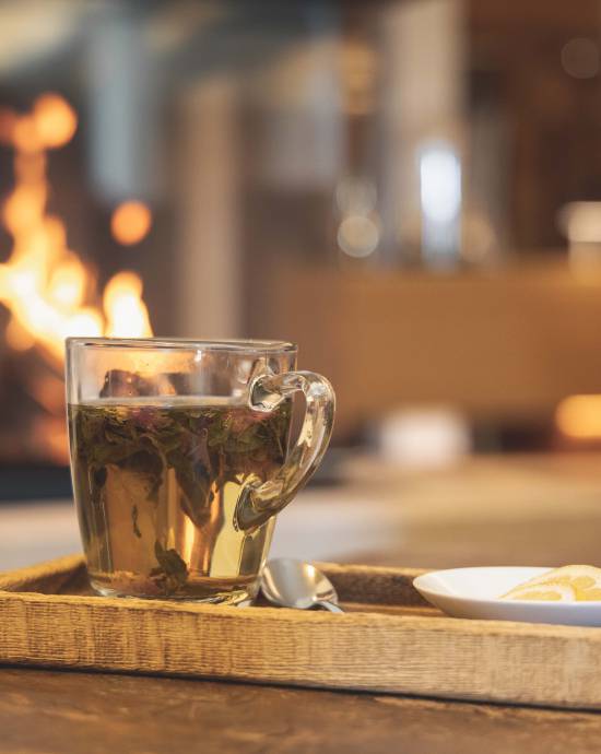 Eine gläserne Tasse mit Tee steht bei warmer Beleuchtung auf einem Holztablett.