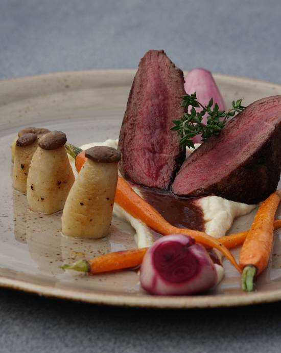 Nahaufnahme einer Mahlzeit aus Steak und Gemüse, welches ansehnlich auf einem naturfarbenen Teller platziert ist.