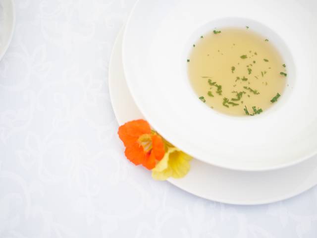 Gemüsebrühe auf einem weißen Teller mit Blüten verziert.