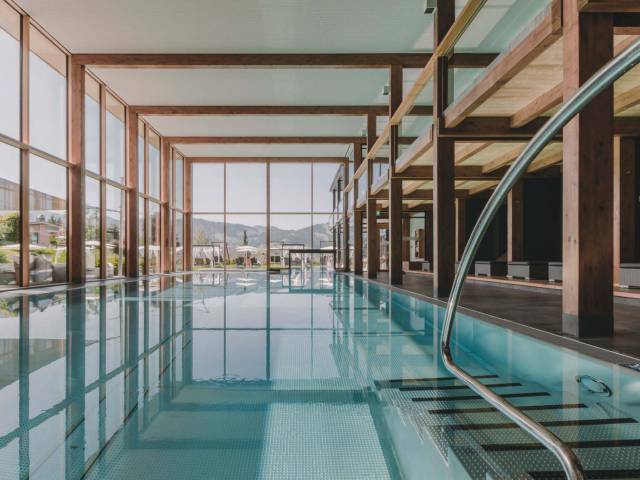 Langer Pool in einem modernen Wellnessbereich mit Holzbalken und großer Fensterfront.