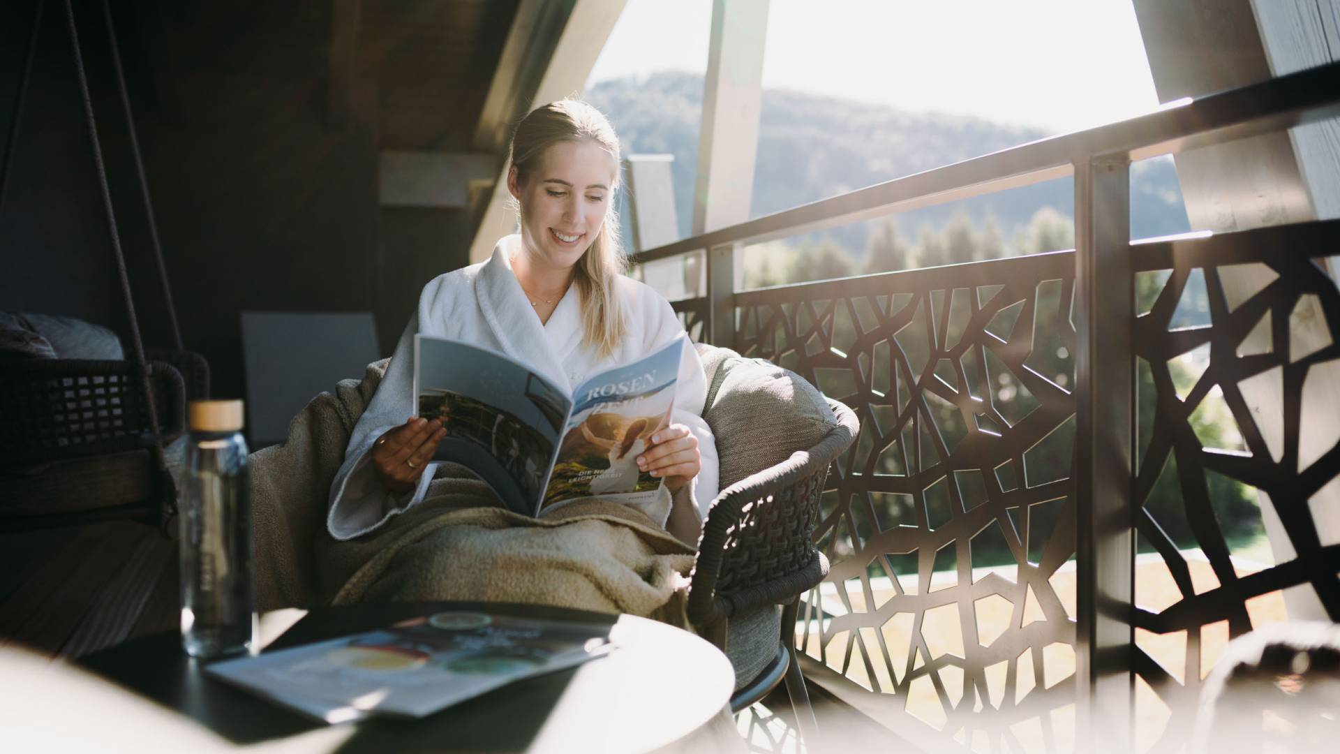 Eine Frau liest ein Magazin auf einem Sessel auf einem Balkon.
