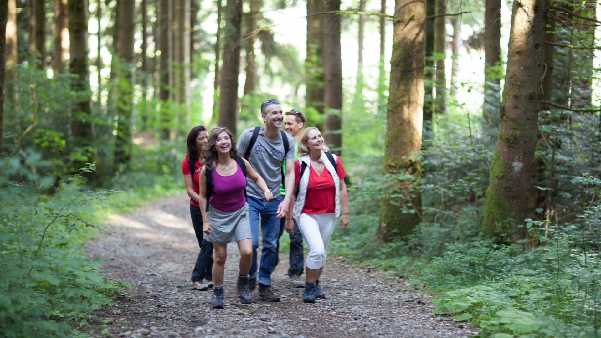 Eine kleine Gruppe wandert lächelnd durch einen Wald als Teil ihres Aktivurlaub im Allgäu.