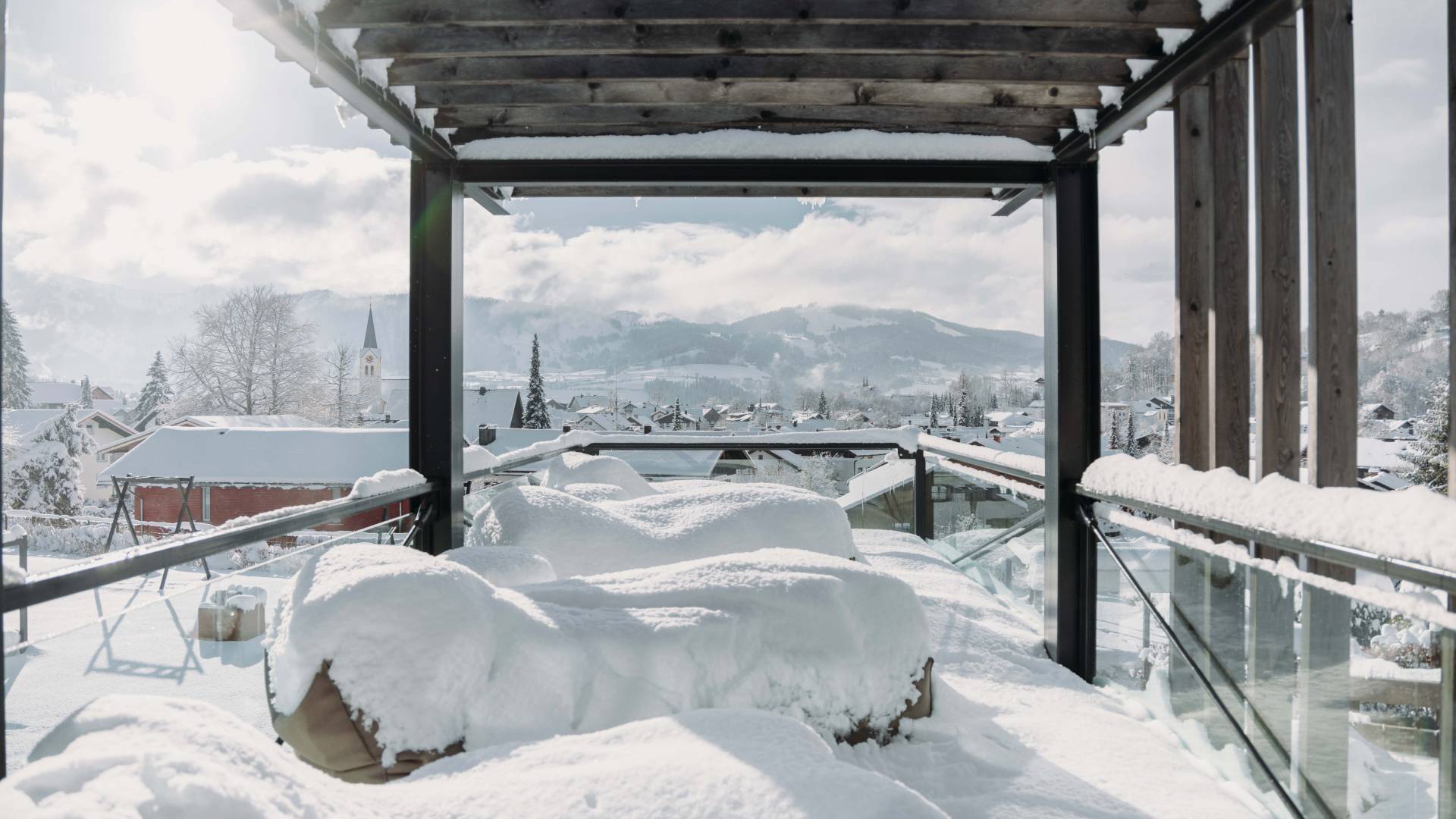 Eine Wellnessterrasse dessen Mobiliar im Winter mit einer Schneeschicht bedeckt ist und Lust auf Winterurlaub in Bayern macht.