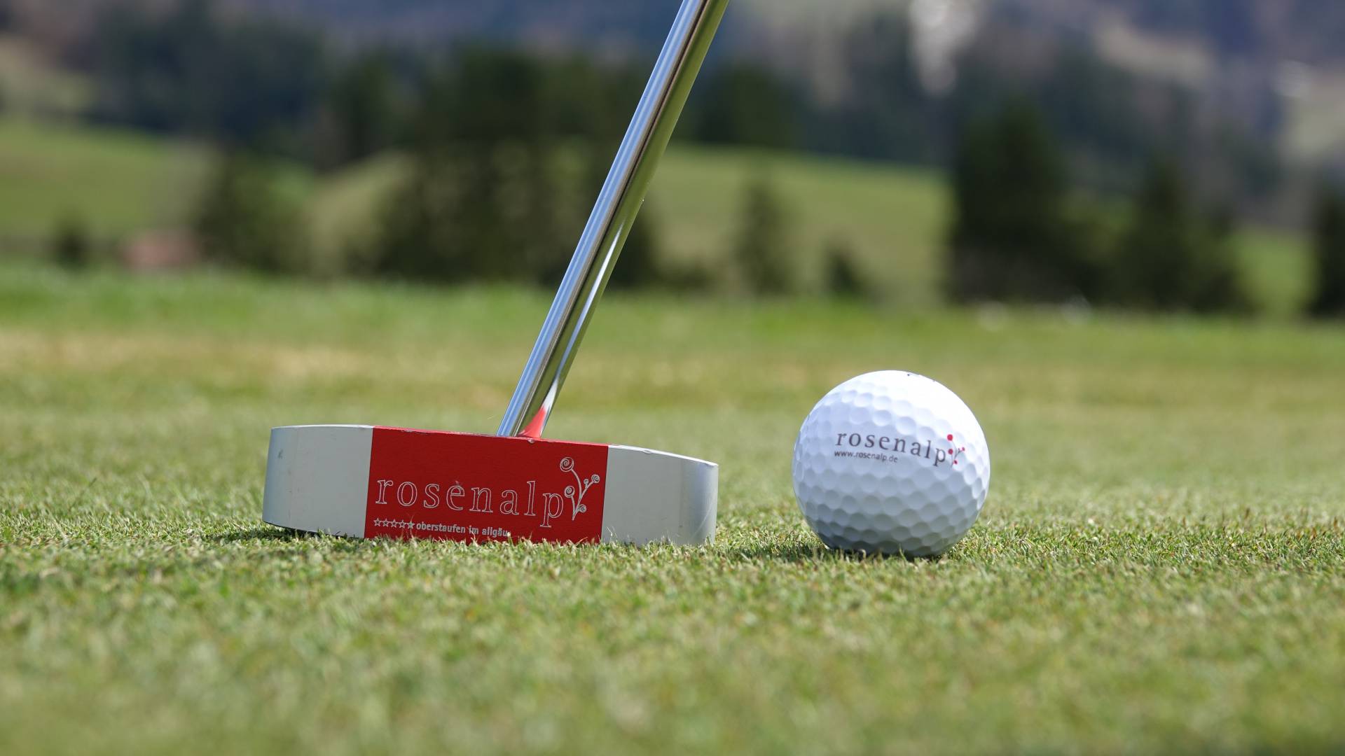 Nahaufnahme eines Putters und Golfballs mit der Aufschrift "rosenalp" auf Rasen als Teil eines Sommerurlaub in Bayern.