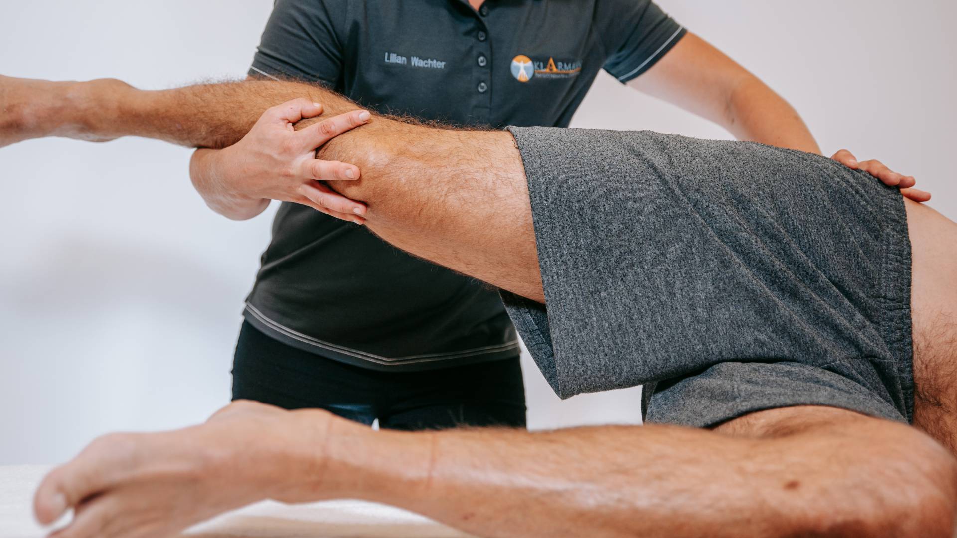 Ein Mann in kurzer, grauer Sporthose bekommt eine physiotherapeutische Behandlung an Bein und Hüfte.