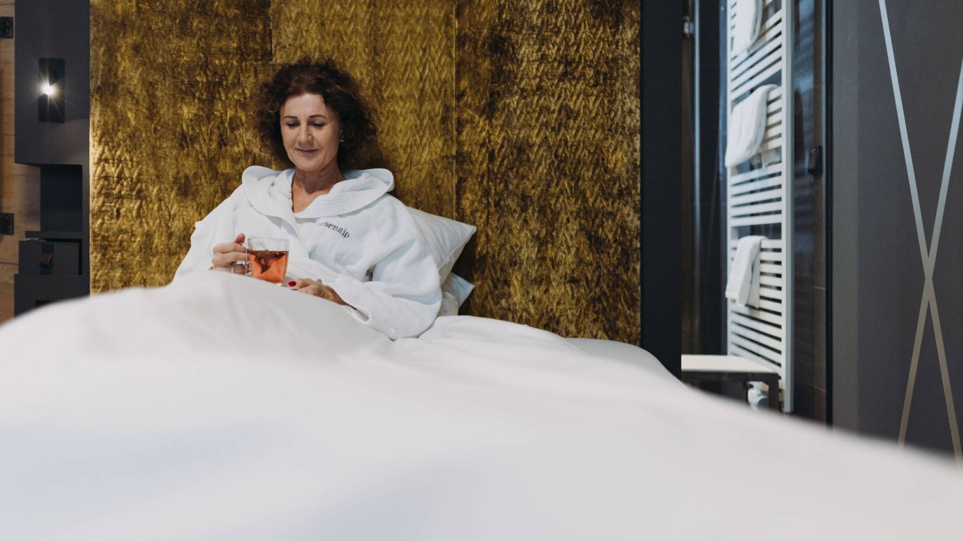 Eine Frau liegt mit einem Tee auf einer Liege mit goldenem Rückenteil als Teil ihres Kururlaub in Bayern.